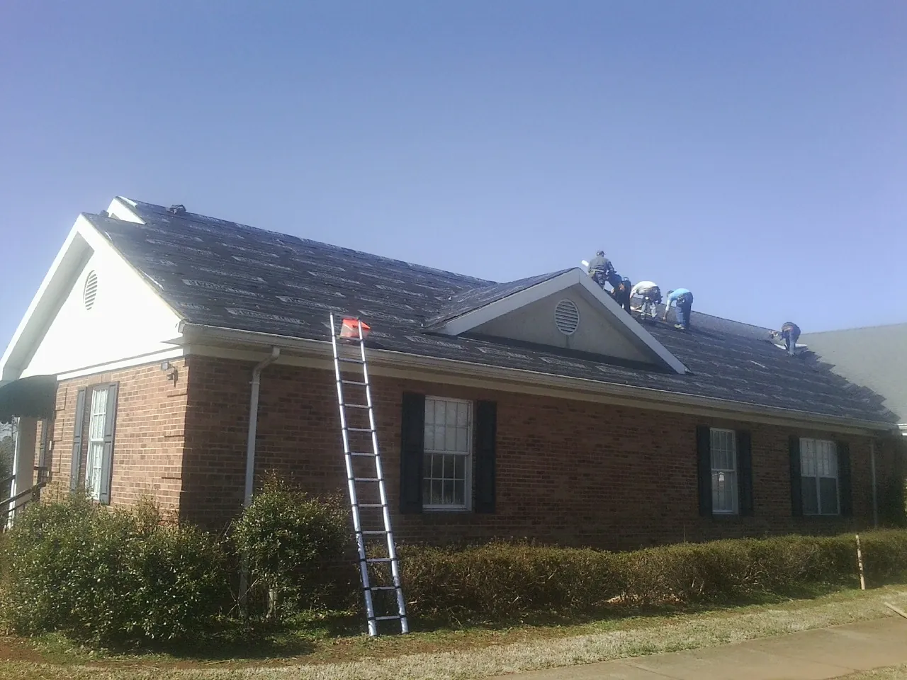 Crew tearing shingles off a brick ranch roof with a ladder set — Metal Roof Repair work by our crew in Hainesport