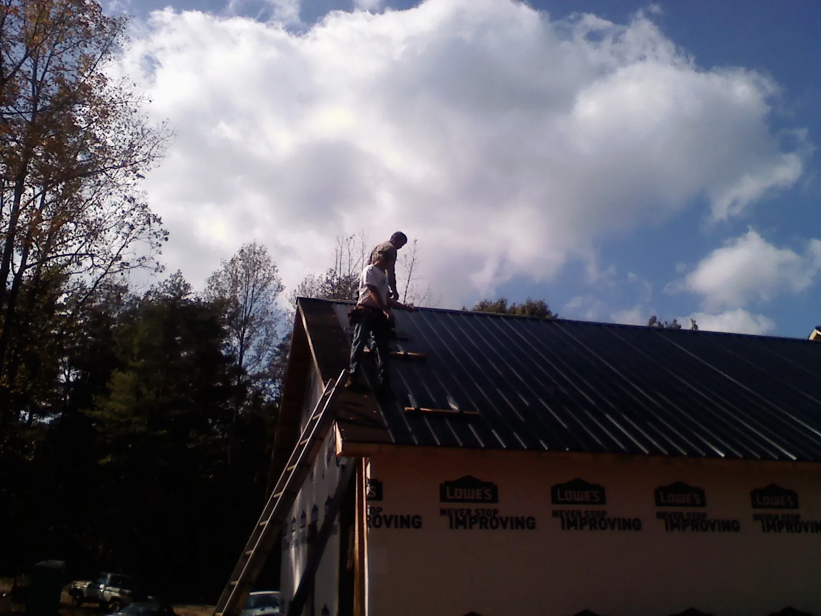 Roofer fastening dark metal panels high against a cloudy sky, from a Roof Inspection job in Hainesport