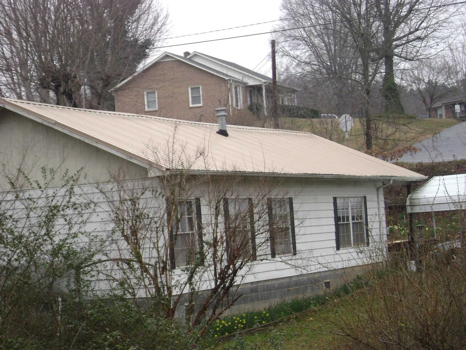 Tan metal roof on a white sided house set into a hillside — Commercial Roofing by Roofing Brothers in Hainesport